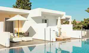 En hvit bygning med terrasse og solsenger ved et basseng. (AI-generert tekst)