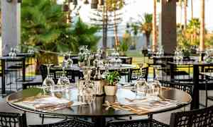 En utendørsrestaurant med bord dekket med glass og bestikk. (AI-generert tekst)