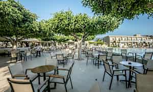 Utendørsområde med stoler og bord under trær nær et basseng. (AI-generert tekst)