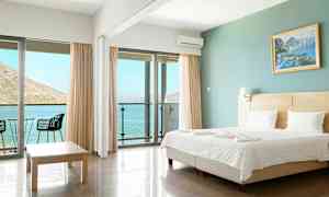 Et hotellrom med en dobbeltseng, glassdører som fører til en balkong med utsikt over havet. (AI-generert tekst)