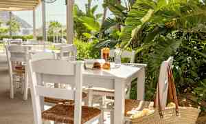 Et bord med hvite stoler, plassert utendørs ved grøntområder, med bok, solbriller og drikke. (AI-generert tekst)