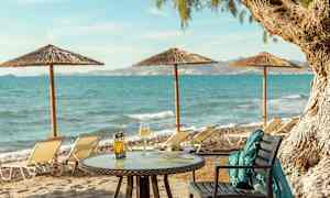 Bord med mat og drikke på en sandstrand med havutsikt og solsenger. (AI-generert tekst)