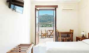 Hotellrom med åpen dør mot en balkong med utsikt over fjell og en landsby. (AI-generert tekst)