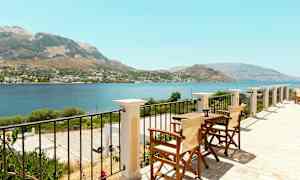 Utsikt fra en terrasse med bord og stoler over hav og fjell. (AI-generert tekst)