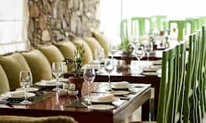 Et bord dekket med glass og tallerkener i en restaurant med grønne stoler og grønne puter. (AI-generert tekst)