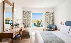 Et hotellrom med balkong, møbler inkludert seng, skrivebord, stol og lenestol. (AI-generert tekst)