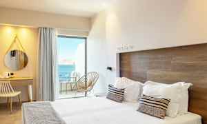 Et hotellrom med moderne interiør, en dobbeltseng, et skrivebord og utsikt over havet fra en balkong. (AI-generert tekst)