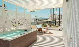 En terrasse med boblebad, solsenger og utsikt mot palmer og bygninger i bakgrunnen. (AI-generert tekst)