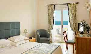 Et soverom med en dobbeltseng, en stol, et skrivebord og en balkong med utsikt over havet. (AI-generert tekst)