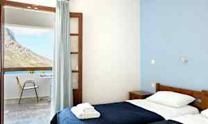 Et rom med to enkeltsenger og stort vindu med utsikt over en uteplass og en fjellside. (AI-generert tekst)