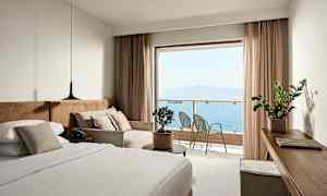 Et hotellrom med en seng, sofa og utsikt over havet fra en balkong. (AI-generert tekst)