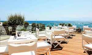 En terrasse med hvite bord og stoler, utsikt over havet. (AI-generert tekst)