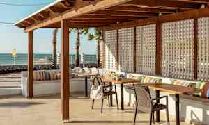 En utendørs terrasse med tremøbler, fargerike puter og havutsikt. (AI-generert tekst)