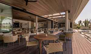 Åpne sitteområder med trebord og flettede stoler under et tak. (AI-generert tekst)