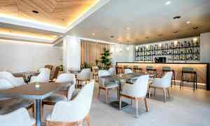 En moderne og lys kafé med bord og stoler samt en velutstyrt bardisk. (AI-generert tekst)