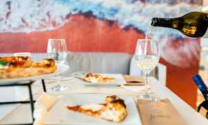 Et bord med pizza og vinglass, bakgrunn med et bilde av stranden. (AI-generert tekst)