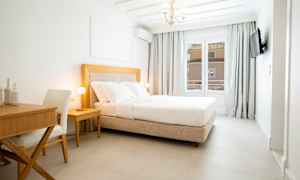 Et lyst hotellrom med en komfortabel dobbeltseng, et skrivebord og en stol. (AI-generert tekst)