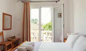 Et lyst soverom med hvite vegger, en seng med hvitt sengetøy og en balkong utenfor glassdører. (AI-generert tekst)