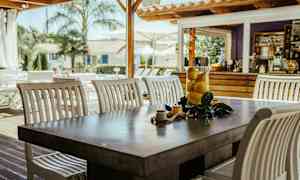 Et bord med hvite stoler og en glassbeholder med sitroner står utendørs nær en trebygning. (AI-generert tekst)