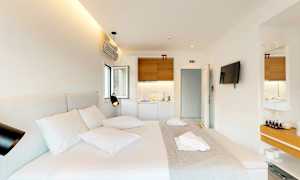 Et moderne hotellrom med en dobbeltseng, en veggmontert TV og en liten kjøkkenkrok. (AI-generert tekst)