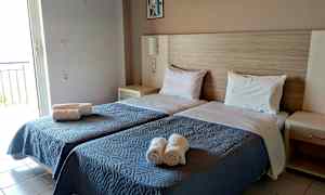 Rommet har to enkeltsenger med blå sengetepper og hvite puter, samt rullede håndklær plassert på sengen. (AI-generert tekst)