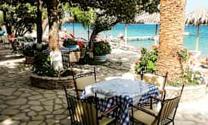 En utendørs servering ved en strand, med bord og stoler under trær. (AI-generert tekst)