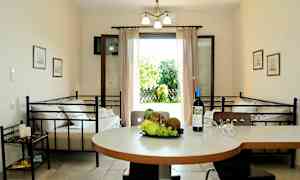 Et innendørs miljø med et bord med frukt og en vinflaske, to senger og en åpen dør som leder til en hage. (AI-generert tekst)