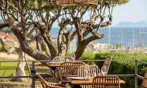 Uteservering med rottingstoler og utsikt over havet. (AI-generert tekst)