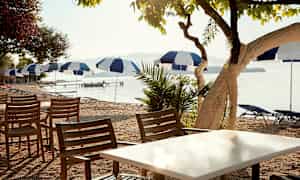 Utemøbler med stoler og bord nær en strand med parasoller. (AI-generert tekst)