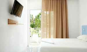 Et lyst rom med en seng, en veggmontert TV og en balkong med utsikt. (AI-generert tekst)