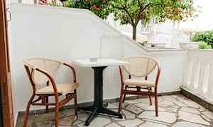 En liten uteplass med to stoler og et bord foran et appelsintre. (AI-generert tekst)