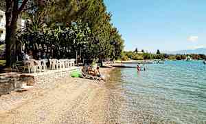 En strand med solsenger, badebrygge og klart blått vann. (AI-generert tekst)