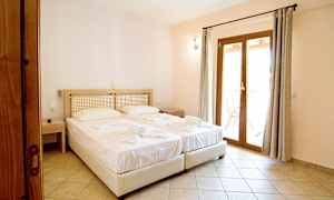 To senger med hvite laken i et hotellrom med dører som fører til balkongen. (AI-generert tekst)