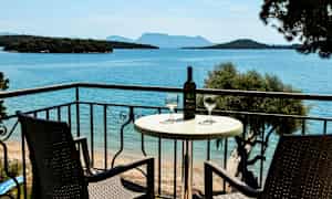 To stoler og et bord med en vinflaske og glass på en balkong med utsikt over havet. (AI-generert tekst)