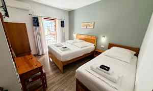 Hotellrom med to enkeltsenger, et skrivebord og en balkong. (AI-generert tekst)