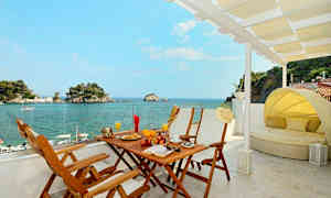 Utsikt fra en terrasse med spisebord og solseng mot havet og små øyer. (AI-generert tekst)