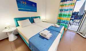 Et hotellrom med to enkeltsenger, blå sengetepper og et maleri over. (AI-generert tekst)