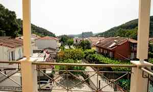Utsikt fra en balkong over hus med tegltak og grøntområder samt fjell i bakgrunnen. (AI-generert tekst)