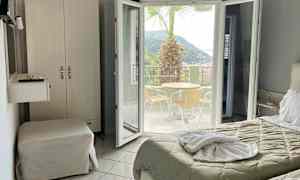 Hotellrom med utsikt mot en terrasse med bord, stoler og en palme. (AI-generert tekst)