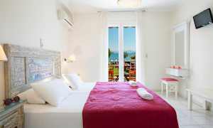 Et lyst og luftig hotellrom med en dobbeltseng utstyrt med hvitt sengetøy og et lilla teppe. Vindu med utsikt over havet og en balkong. (AI-generert tekst)