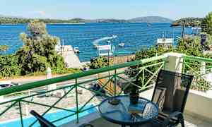 Utsikt fra en balkong mot en blå havsbukt med båter og frodige omgivelser. (AI-generert tekst)
