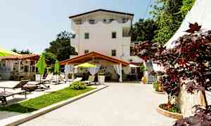 Utendørs miljø med en treetasjes bygning, solsenger og grønne parasoller. (AI-generert tekst)