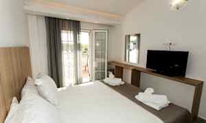 Et hotellrom med en dobbeltseng, en TV på en trebenk og en balkong med utsikt. (AI-generert tekst)