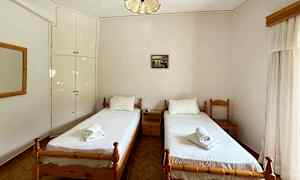 Bilde av et hotellrom med to enkeltsenger og hvitt sengetøy, plassert mot en lys vegg med et lite veggskap. (AI-generert tekst)