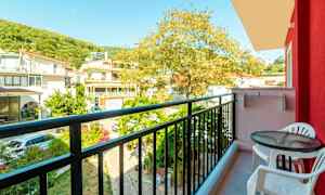 Utsikt fra en balkong med et bord og to stoler samt omkringliggende bygninger og trær. (AI-generert tekst)