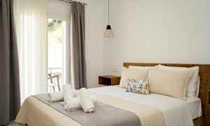 Interiør av et soverom med en oppredt seng, tre sammenrullede håndklær og en balkongdør med gardiner. (AI-generert tekst)