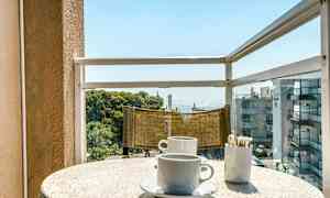 En balkong med utsikt over havet. På bordet står det to kaffekopper og en beholder med sukkerposer. (AI-generert tekst)