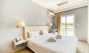 Moderne møblert hotellrom med dobbeltseng og hvite laken. Vindu med lysinnslipp. (AI-generert tekst)