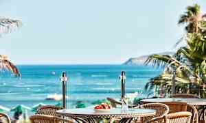 Utsikt over bord med drikkevarer og frukt mot havet. (AI-generert tekst)