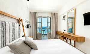 Et lyst og moderne innredet hotellrom med seng og utsikt mot havet fra en balkong. (AI-generert tekst)